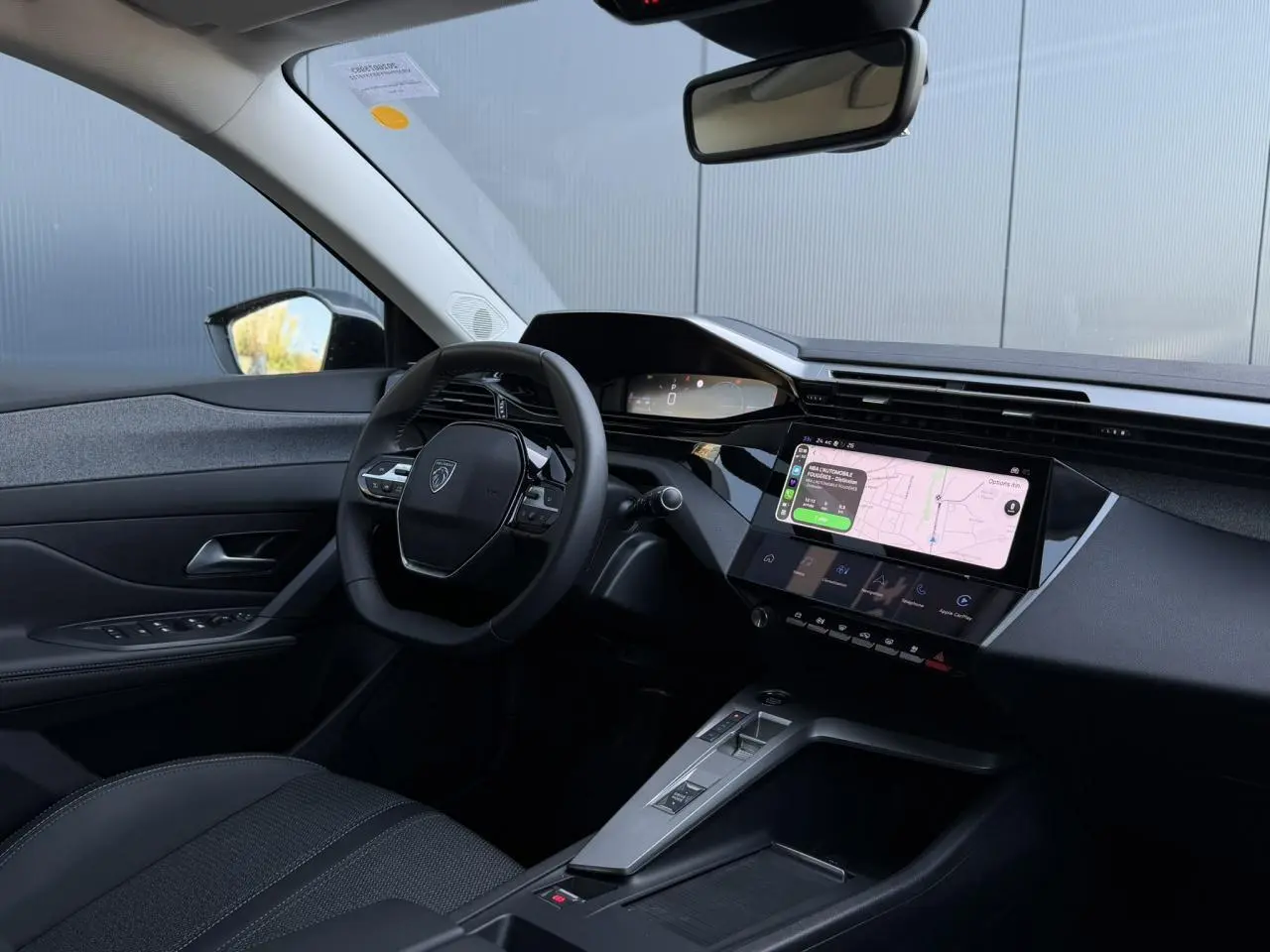 Vue intérieure côté conducteur de la Peugeot 308 Hybrid noire, avec tableau de bord numérique et écran tactile central affichant la navigation.