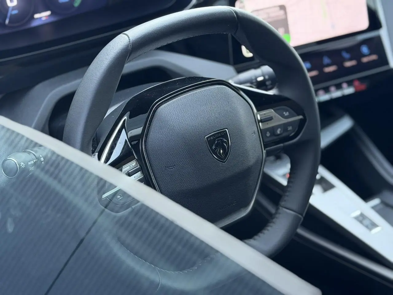 Gros plan sur le volant cuir noir de la Peugeot 308 Hybrid 2025 avec tableau de bord et écran tactile en arrière-plan.