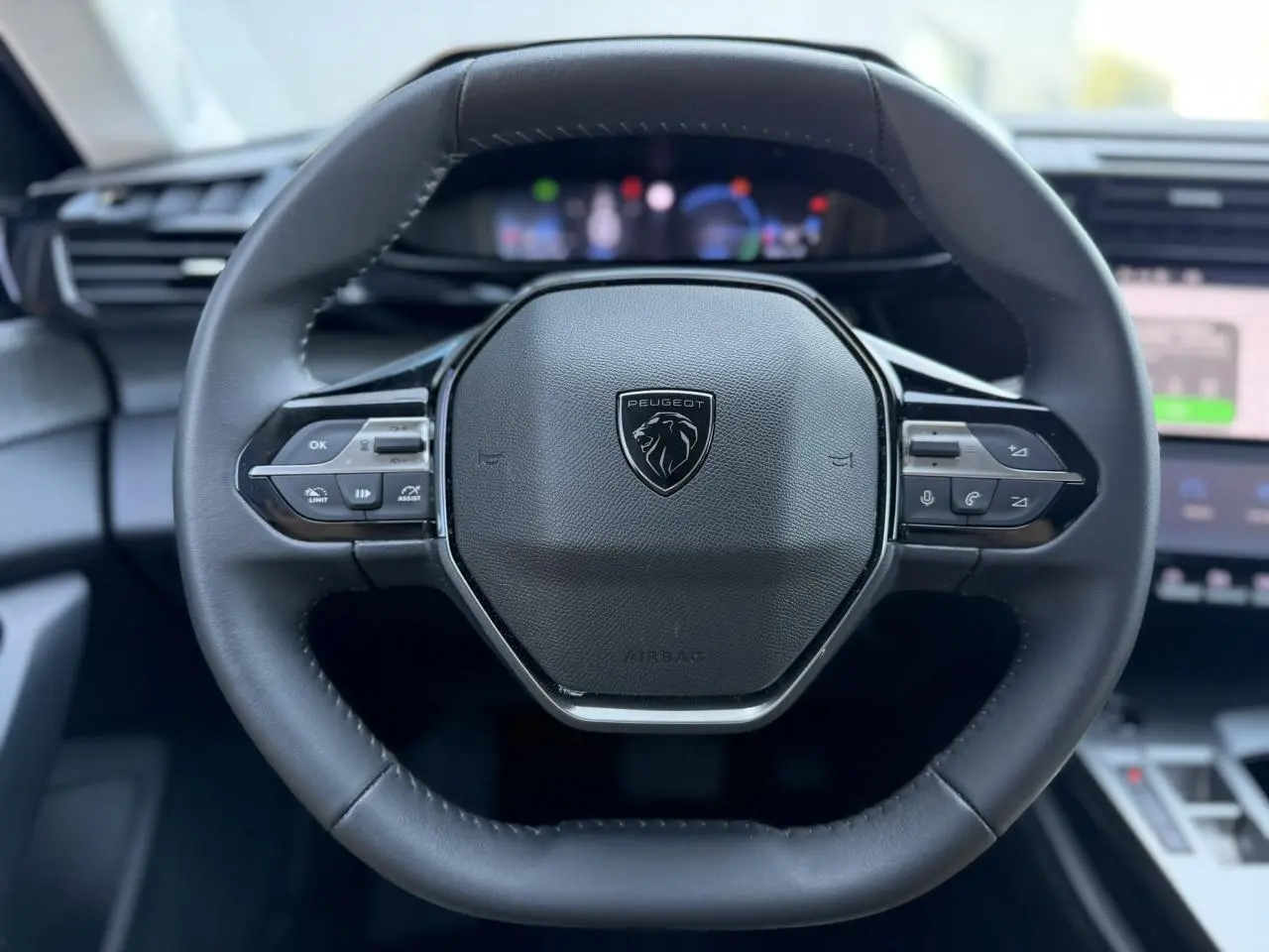 Gros plan sur le volant cuir noir de la Peugeot 308 Hybrid 2025 avec commandes intégrées et logo central lion.