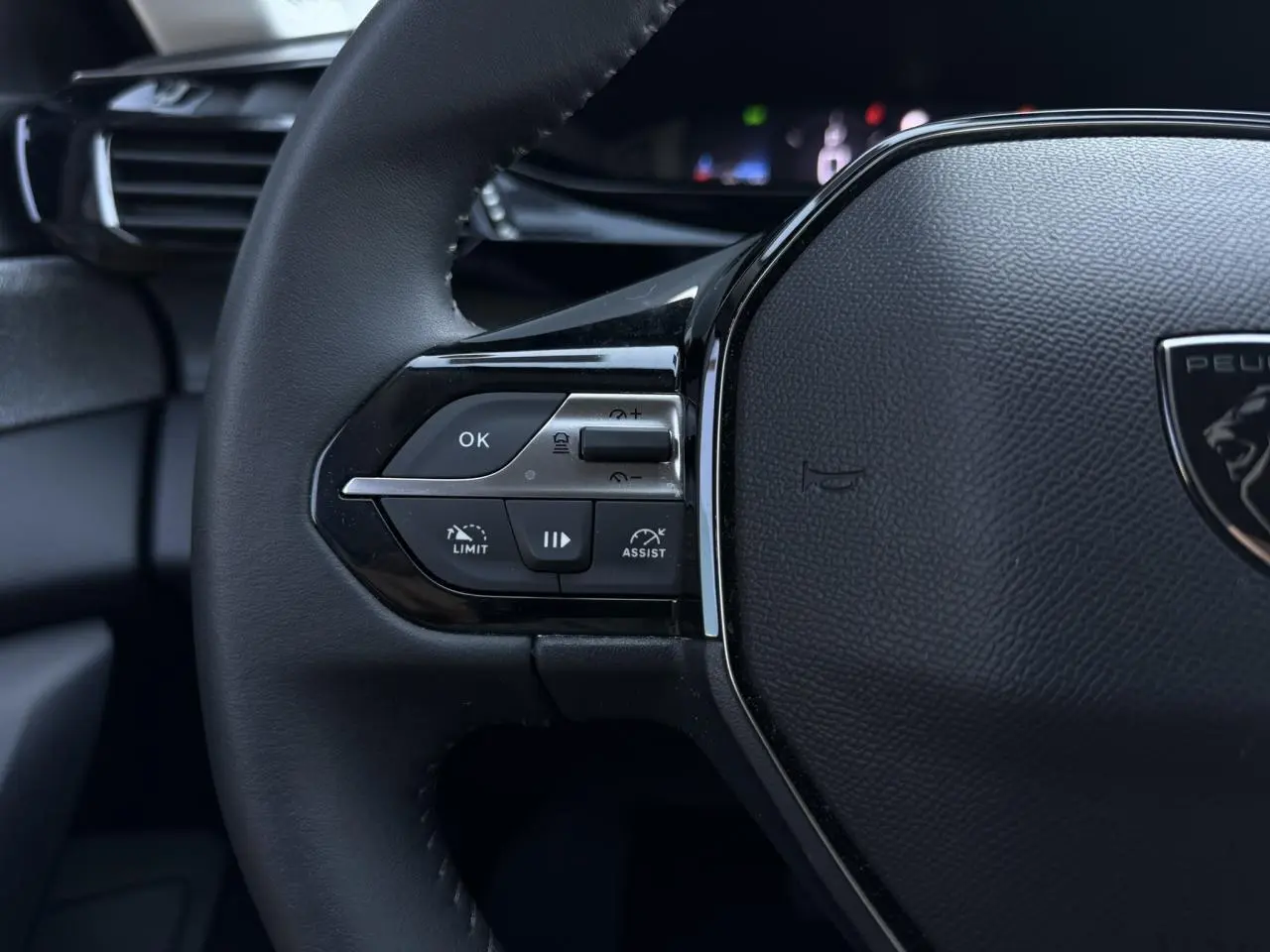Gros plan sur la partie gauche du volant noir de la Peugeot 308 Hybrid avec commandes de régulateur et assistant de conduite.
