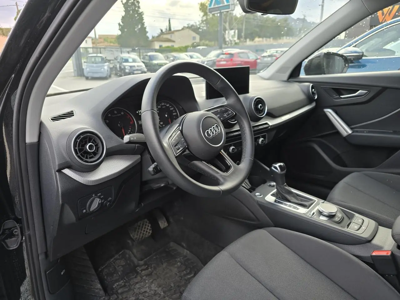 Vue intérieure côté conducteur de l'Audi Q2 2023 noir mythic, avec volant cuir multifonction et console centrale moderne.