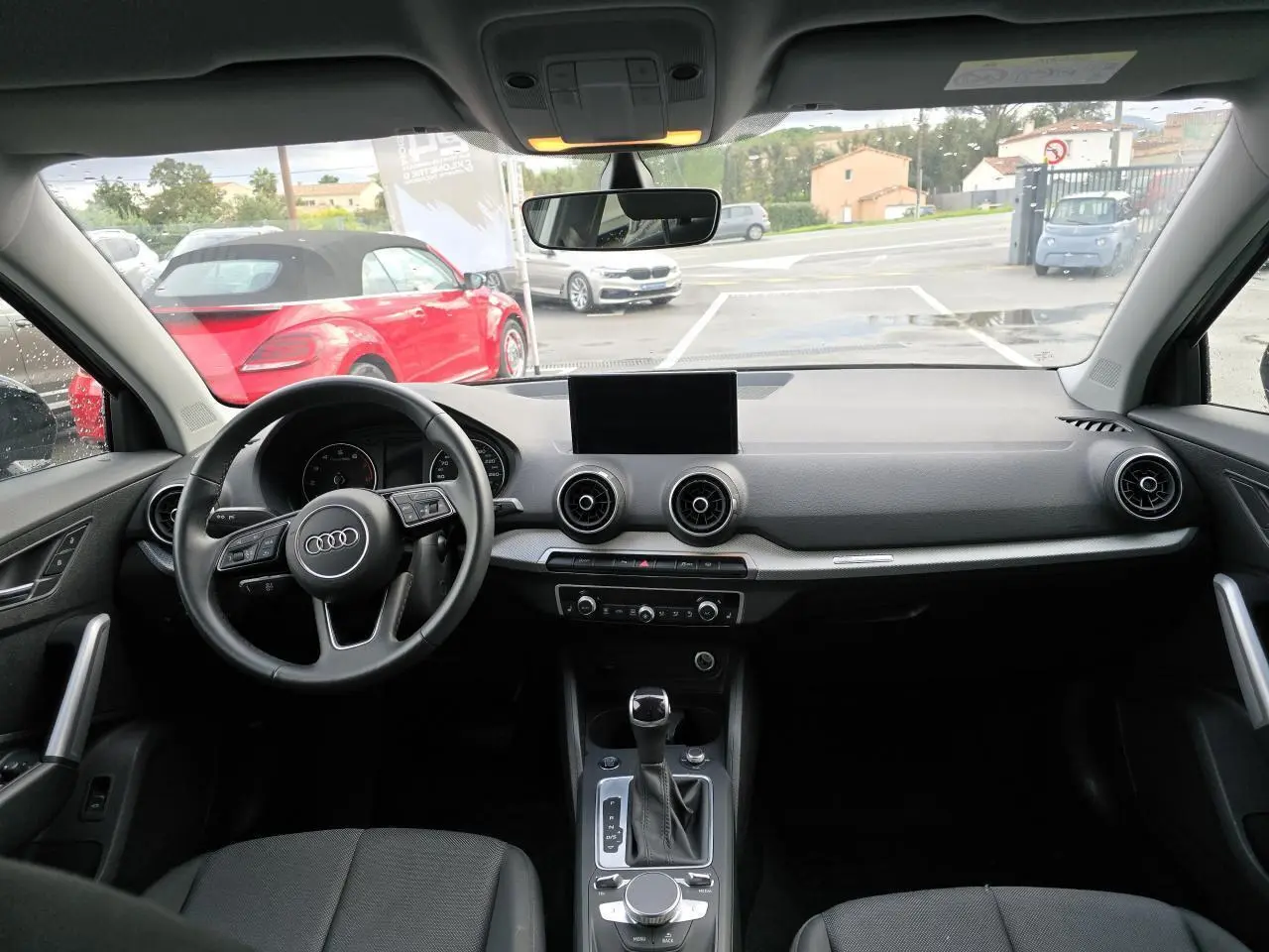 Vue intérieure avant de l'Audi Q2 35 TFSI 2023 avec tableau de bord noir, écran central et volant multifonction cuir.