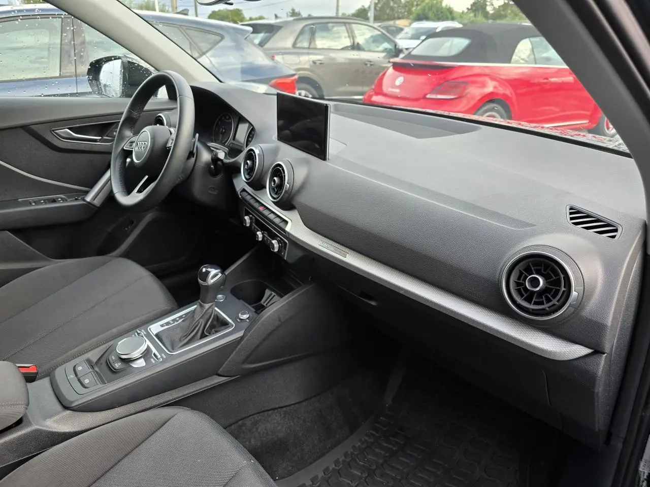 Intérieur avant gauche de l'Audi Q2 35 TFSI 2023 avec tableau de bord noir, écran central et volant multifonction cuir.