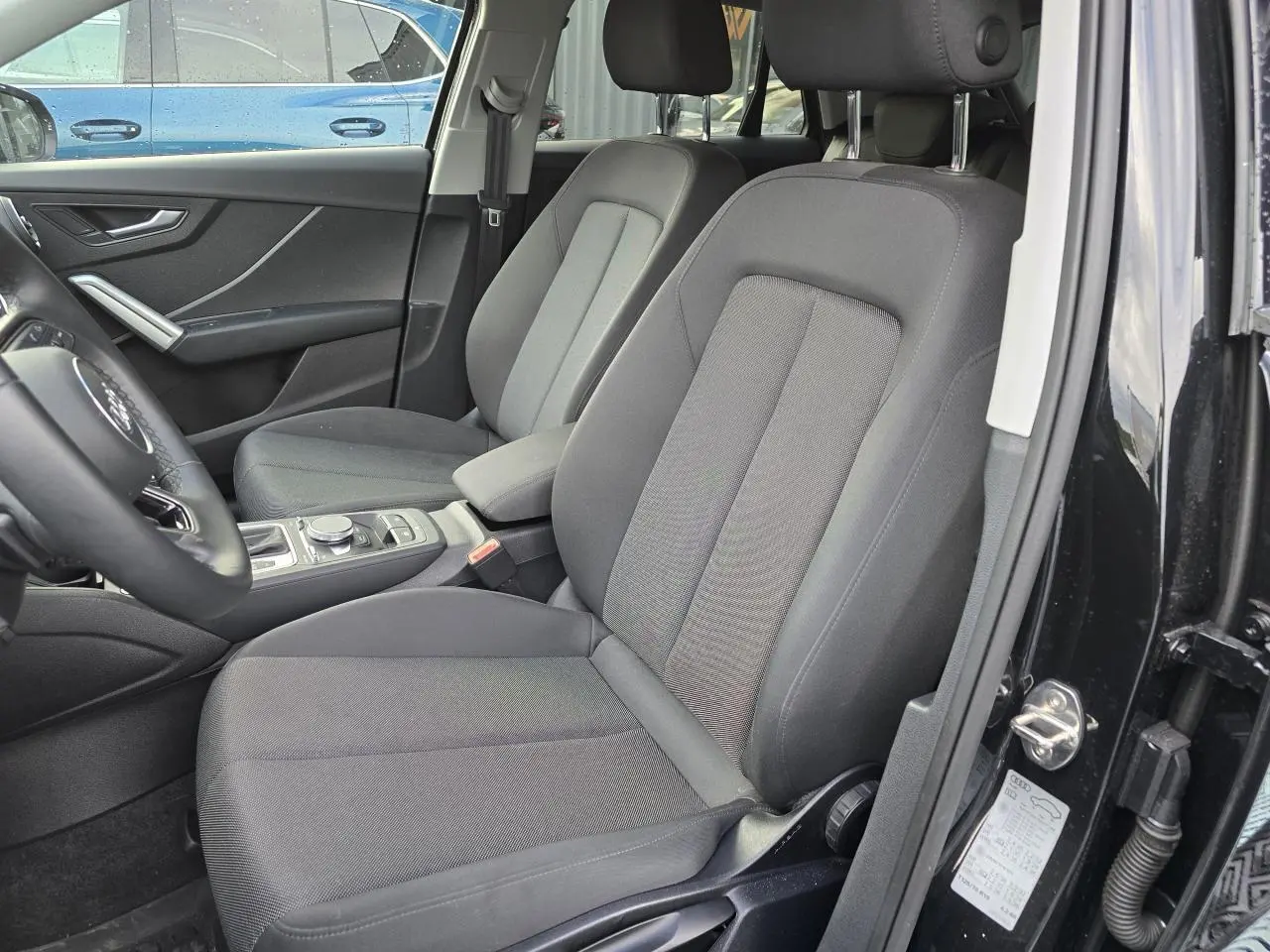 Vue intérieure côté conducteur de l'Audi Q2 35 TFSI noir mythic, montrant les sièges avant en tissu gris et la console centrale.