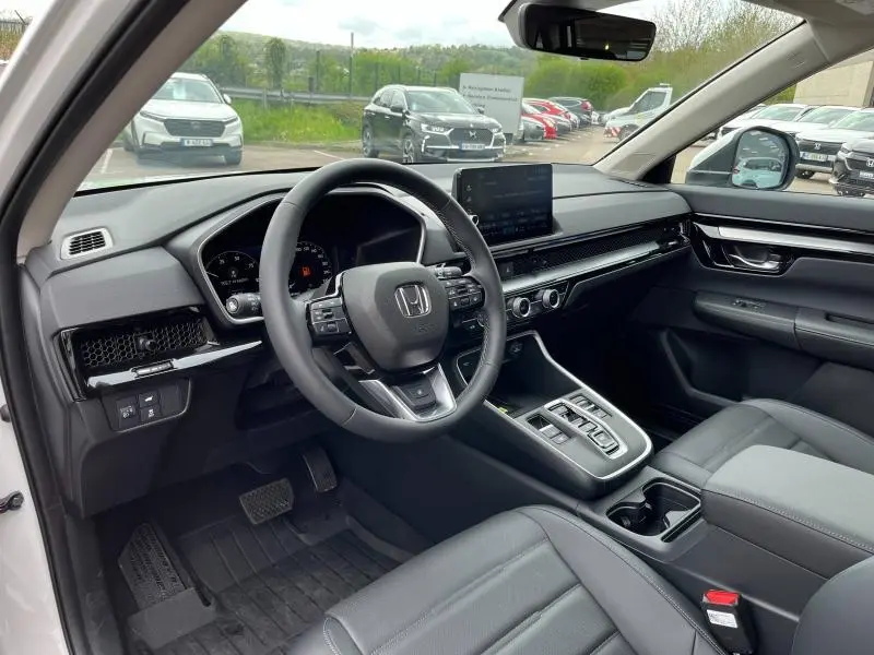 Intérieur du Honda CR-V 2024 blanc Platine nacrée, vue côté conducteur, tableau de bord et volant cuir multifonction.