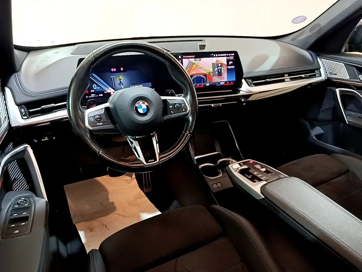 Intérieur noir du BMW X1 xDrive23i M Sport 2023, vue du poste de conduite avec écran tactile et volant cuir multifonctions.
