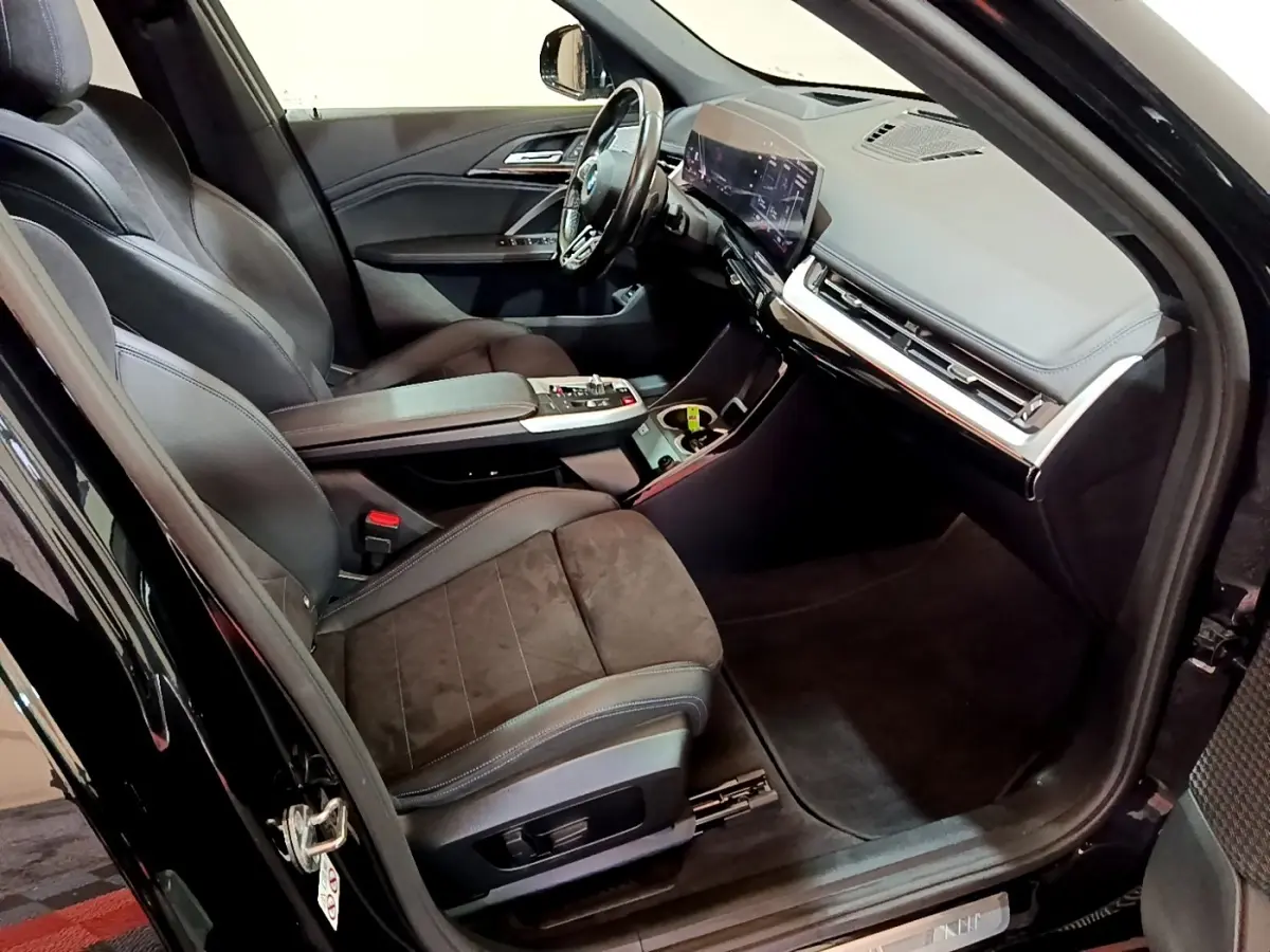 Intérieur noir du BMW X1 xDrive23i M Sport 2023 vu côté conducteur, avec tableau de bord digital et sièges en cuir.