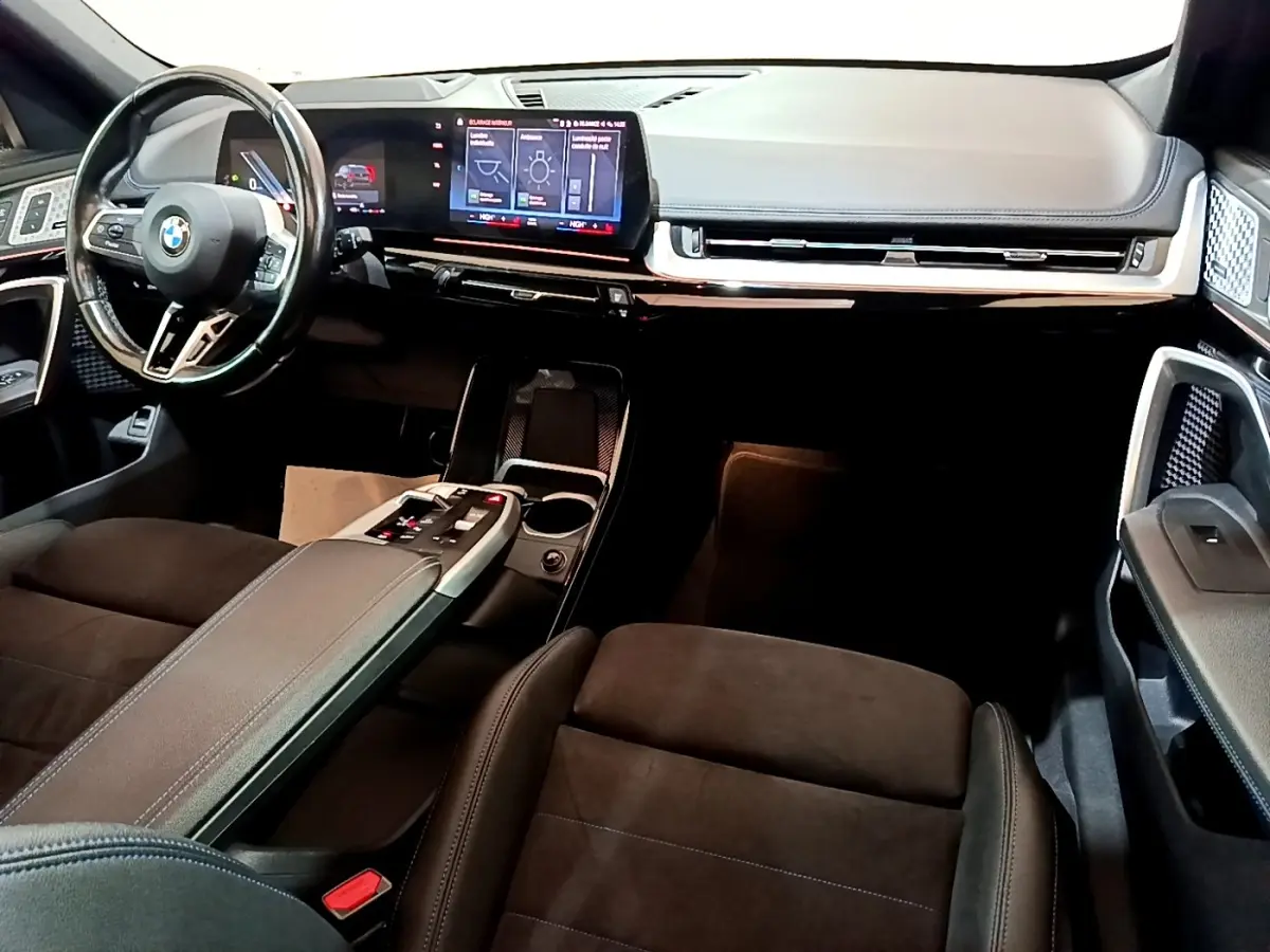 Intérieur avant BMW X1 xDrive23i M Sport 2023, vue du tableau de bord et volant cuir, écran tactile large et console centrale noire.