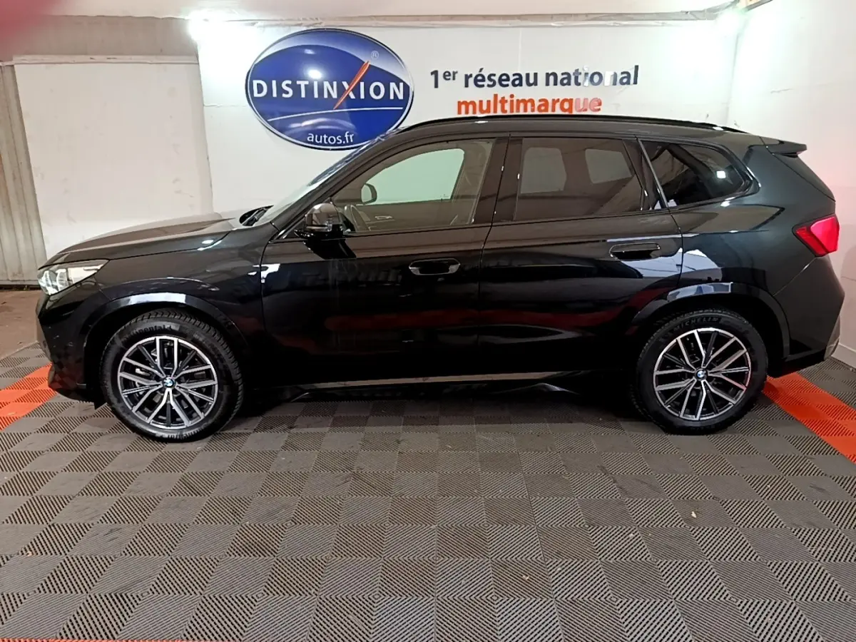 Profil côté gauche d'un BMW X1 noir 2023 xDrive23i M Sport avec jantes alliage en showroom.