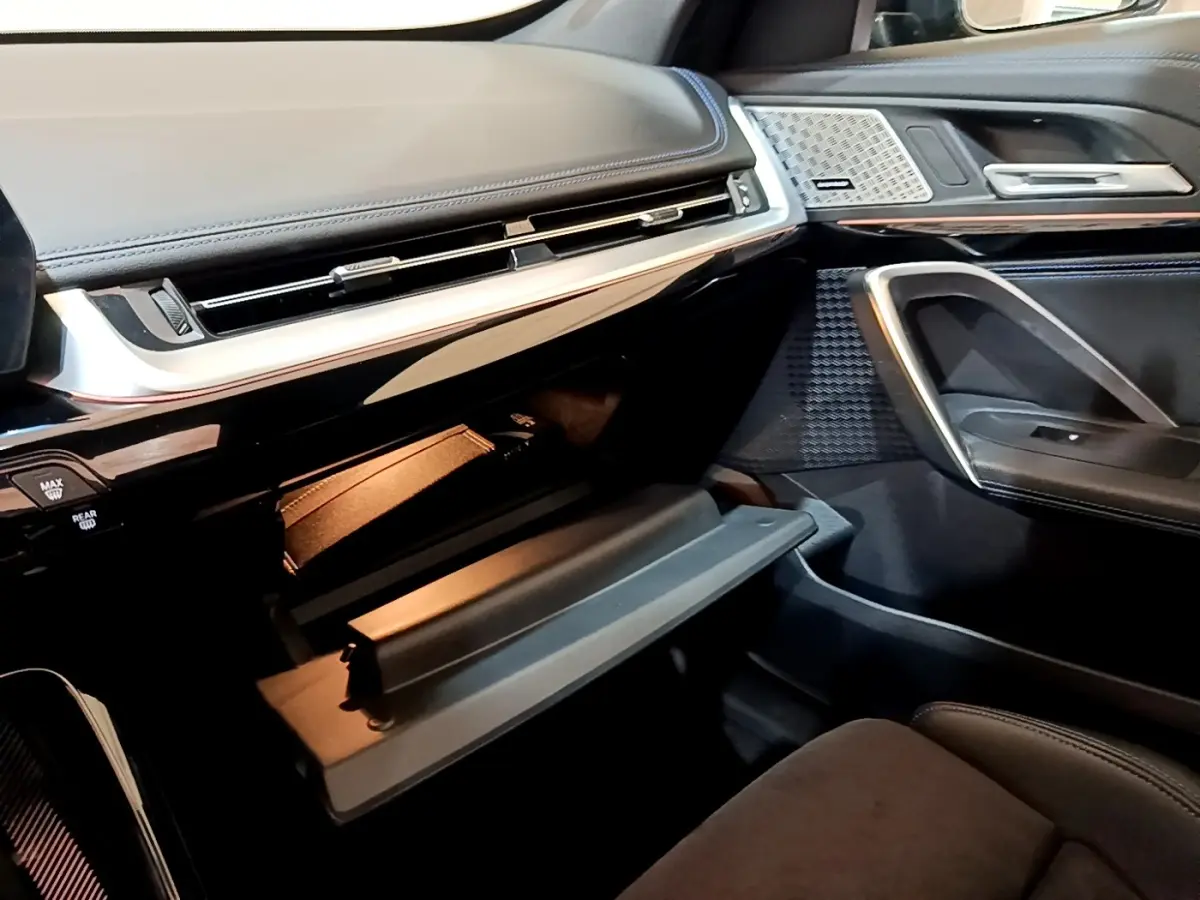 Intérieur BMW X1 xDrive23i M Sport 2023, vue côté passager sur boîte à gants ouverte et garnitures noires élégantes.