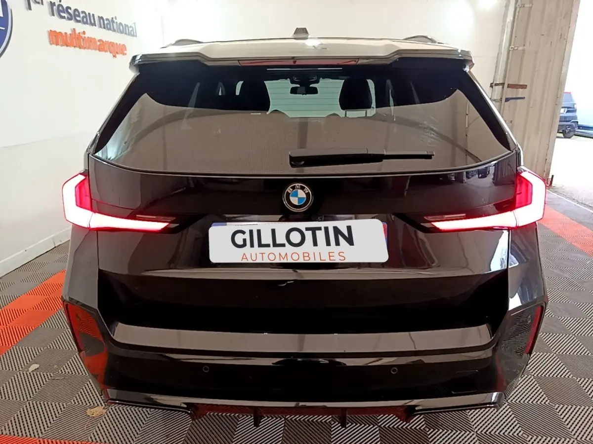 Vue arrière d'un BMW X1 noir 2023 avec feux LED allumés dans un garage intérieur.