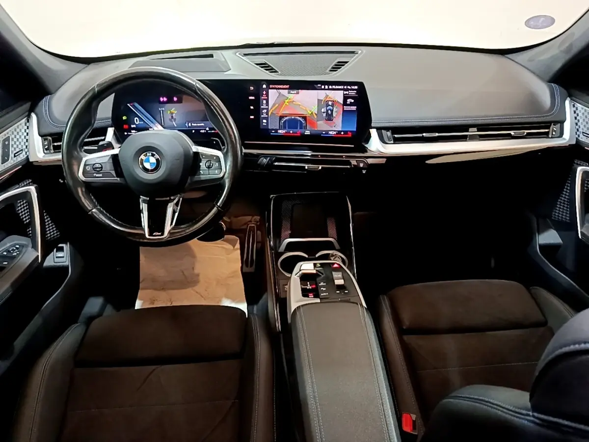 Intérieur noir du BMW X1 xDrive23i M Sport 2023 vu de face, tableau de bord numérique et écran tactile central lumineux.