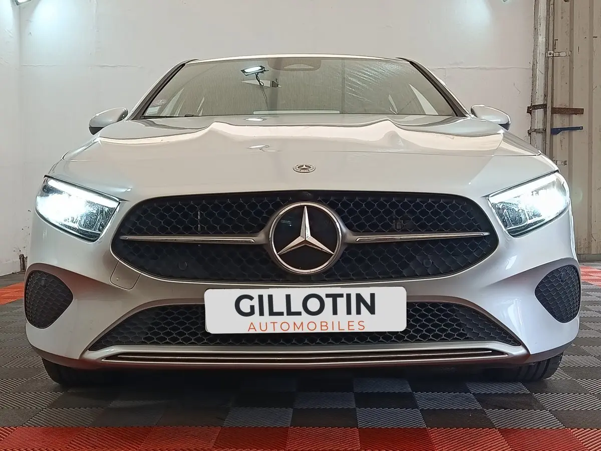 Vue frontale d'une Mercedes Classe A 250 e Business Line gris clair avec phares LED allumés et calandre noire ajourée.