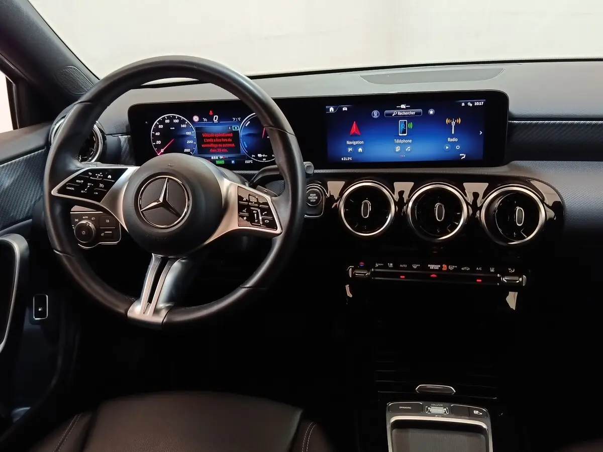 Vue intérieure centrée sur le volant cuir et alu, tableau de bord numérique et écran tactile de la Mercedes Classe A 250 e gris clair.