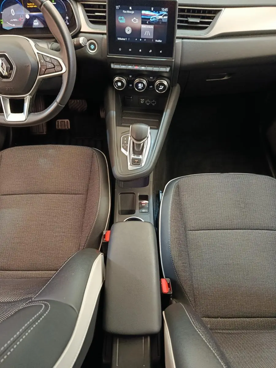 Vue intérieure centrée sur la console centrale et les sièges avant noirs du Renault Captur Intens E-TECH 2021.