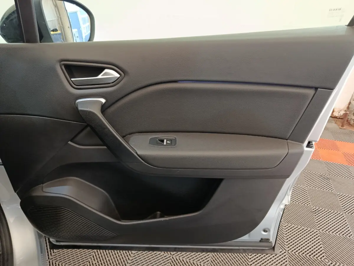 Vue intérieure de la porte avant gauche du Renault Captur gris clair, avec poignée et commande de vitre électrique.
