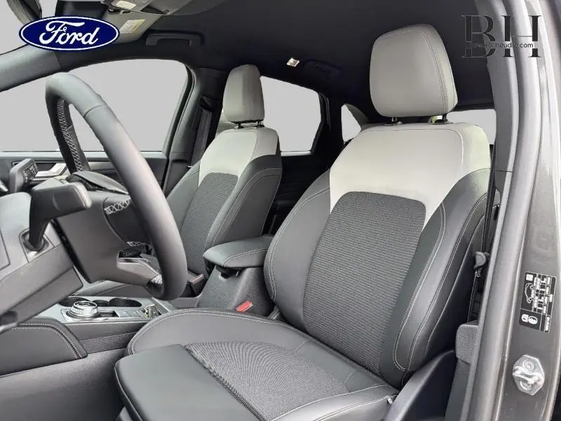 Vue intérieure côté avant droit du Ford Kuga 2026, sièges bi-matière gris clair et foncé avec volant multifonction.