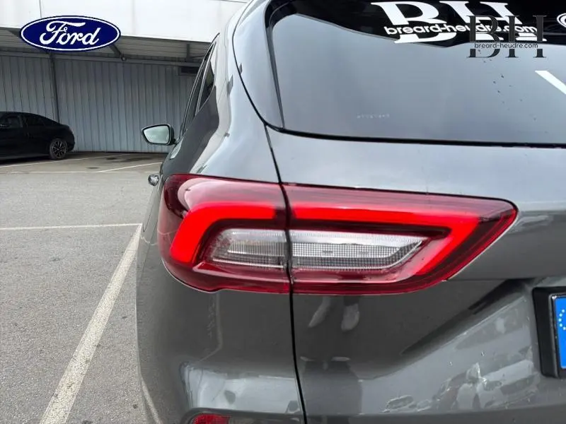 Vue arrière gauche du Ford Kuga 2026 gris Magnetic avec feux arrière LED et logo Ford visible en arrière-plan.