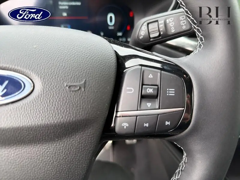 Gros plan sur le volant noir du Ford Kuga 2026 avec commandes multifonctions et coutures blanches visibles.