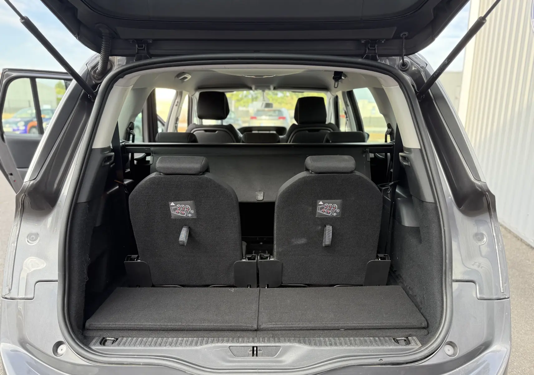 Vue arrière du coffre ouvert d'un Citroën Grand C4 Spacetourer gris, montrant les sièges rabattus et l'intérieur spacieux.
