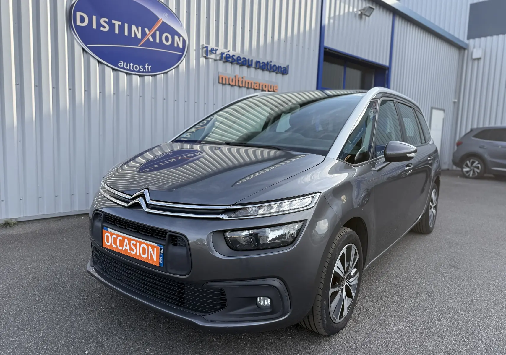 Citroën Grand C4 Spacetourer gris en 3/4 avant droit, avec attelage visible et plaque "OCCASION" orange.