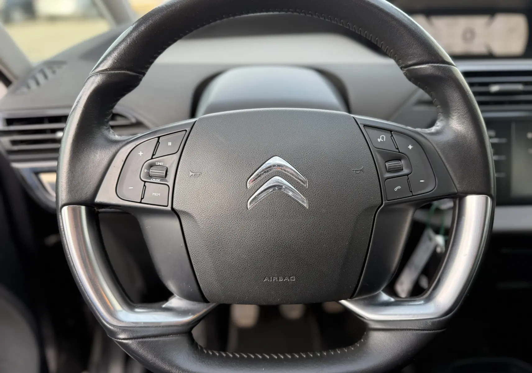 Gros plan sur le volant en cuir noir du Citroën Grand C4 Spacetourer 2019, avec commandes intégrées et logo chromé central.