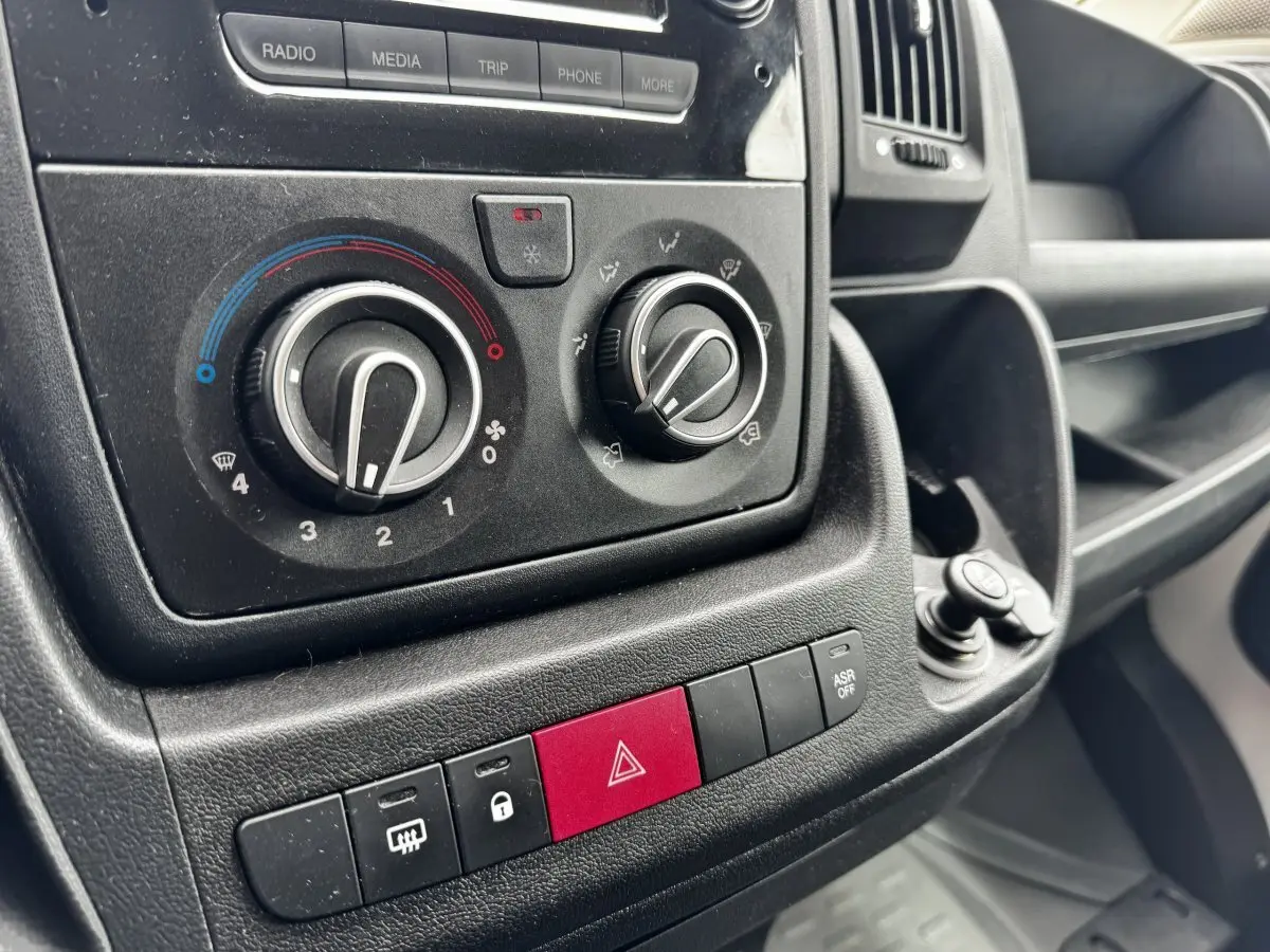 Gros plan sur les commandes de climatisation et les boutons de sécurité du tableau de bord noir du Citroën Jumper blanc.