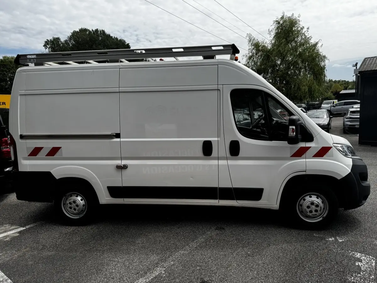 Vue latérale droite d’un utilitaire Citroën Jumper blanc avec marquages rouges et galerie de toit noire.