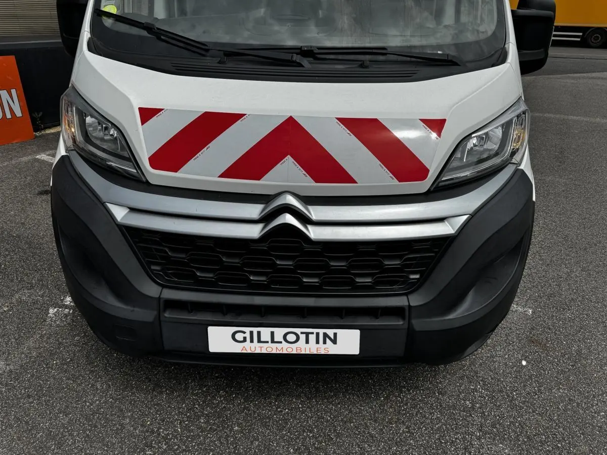Vue frontale rapprochée du Citroën Jumper blanc avec bandes rouges réfléchissantes sur le capot et calandre noire.