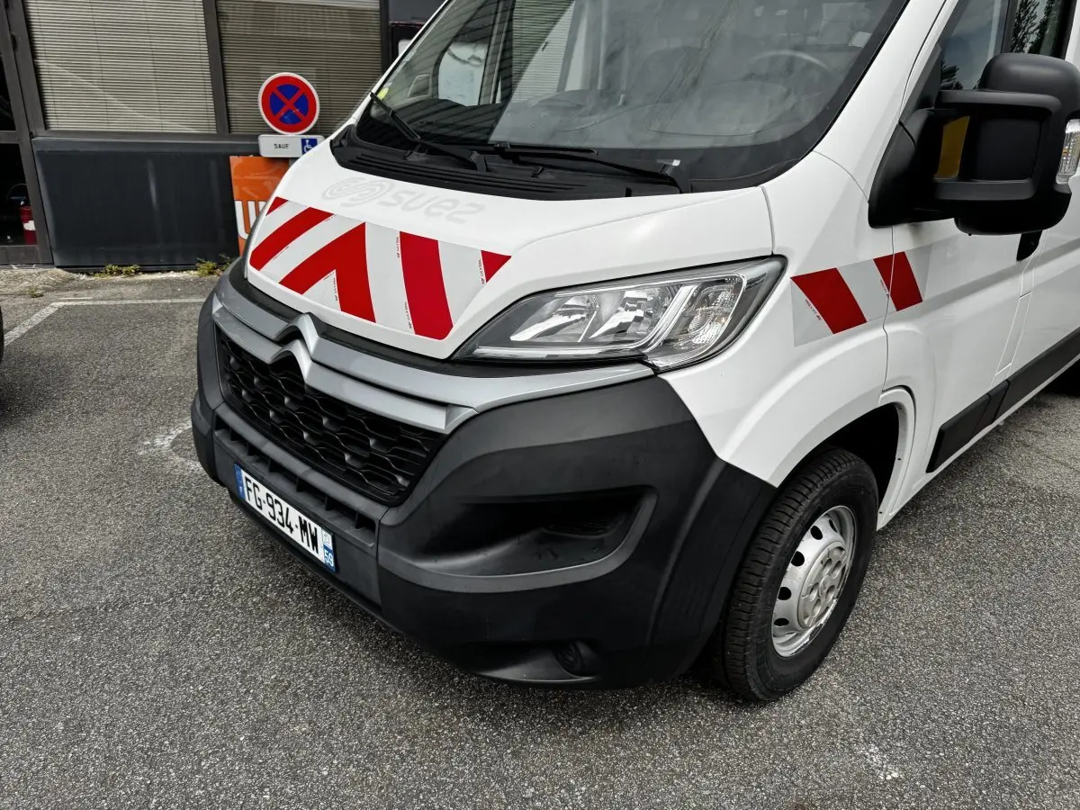 Vue 3/4 avant droit d’un Citroën Jumper blanc avec bandes rouges diagonales sur le capot et l’aile.