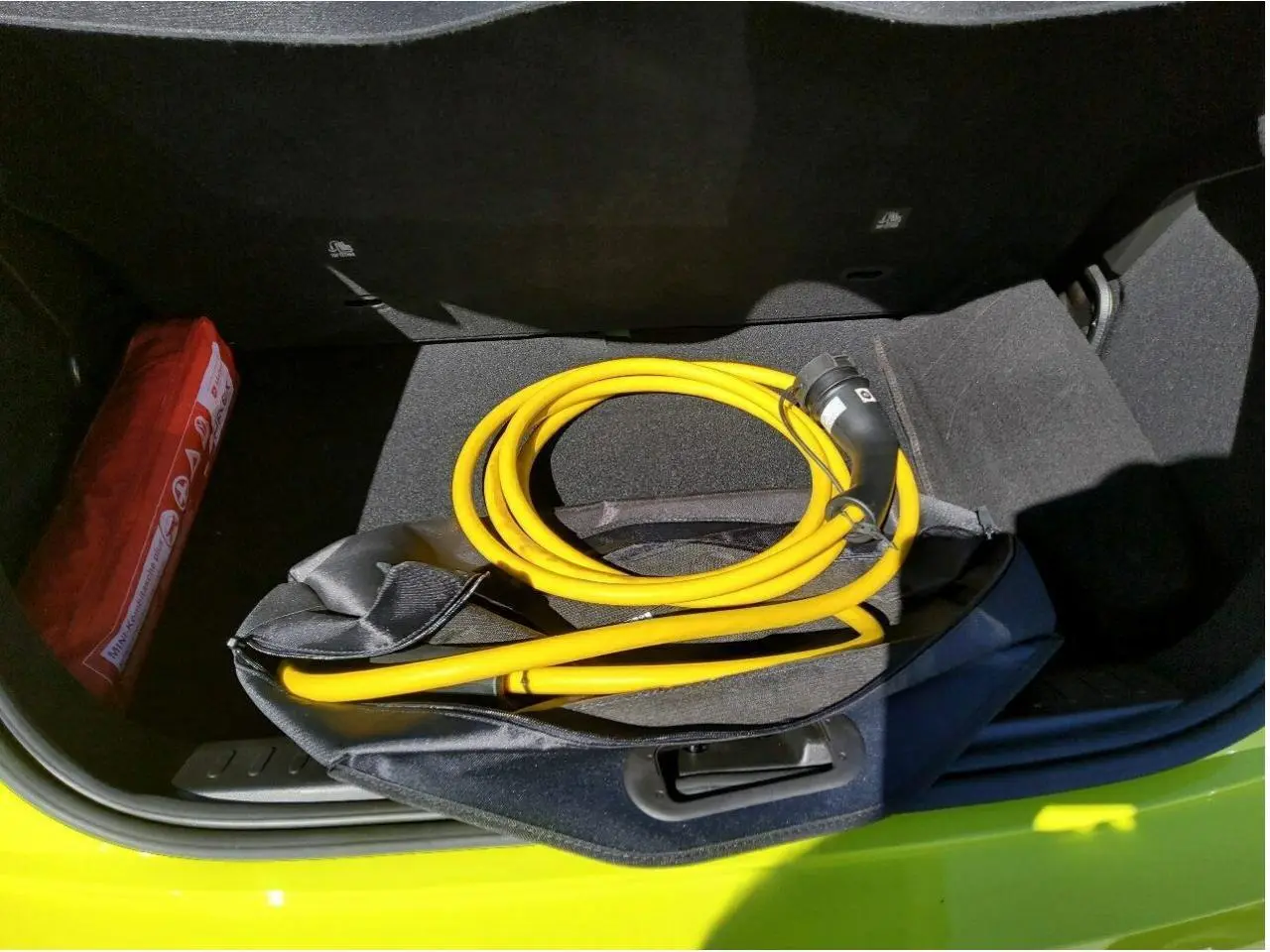 Coffre ouvert vu de dessus d'une Fiat 500 électrique jaune Acid avec câble de recharge jaune enroulé.