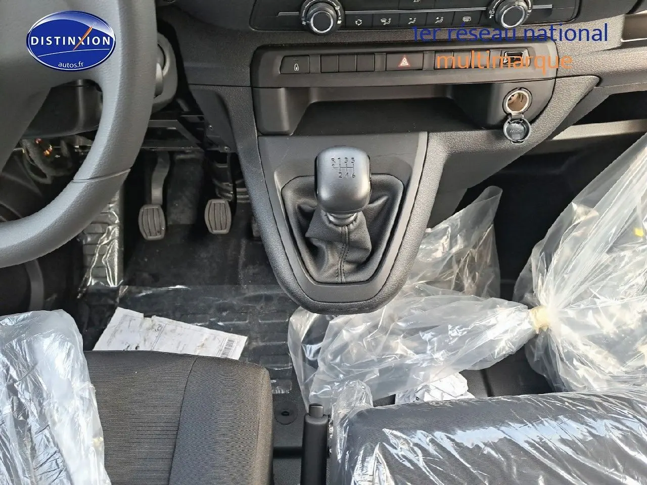 Gros plan sur la console centrale et levier de vitesse manuel du Peugeot Expert blanc, avec sièges noirs protégés par des housses plastiques.