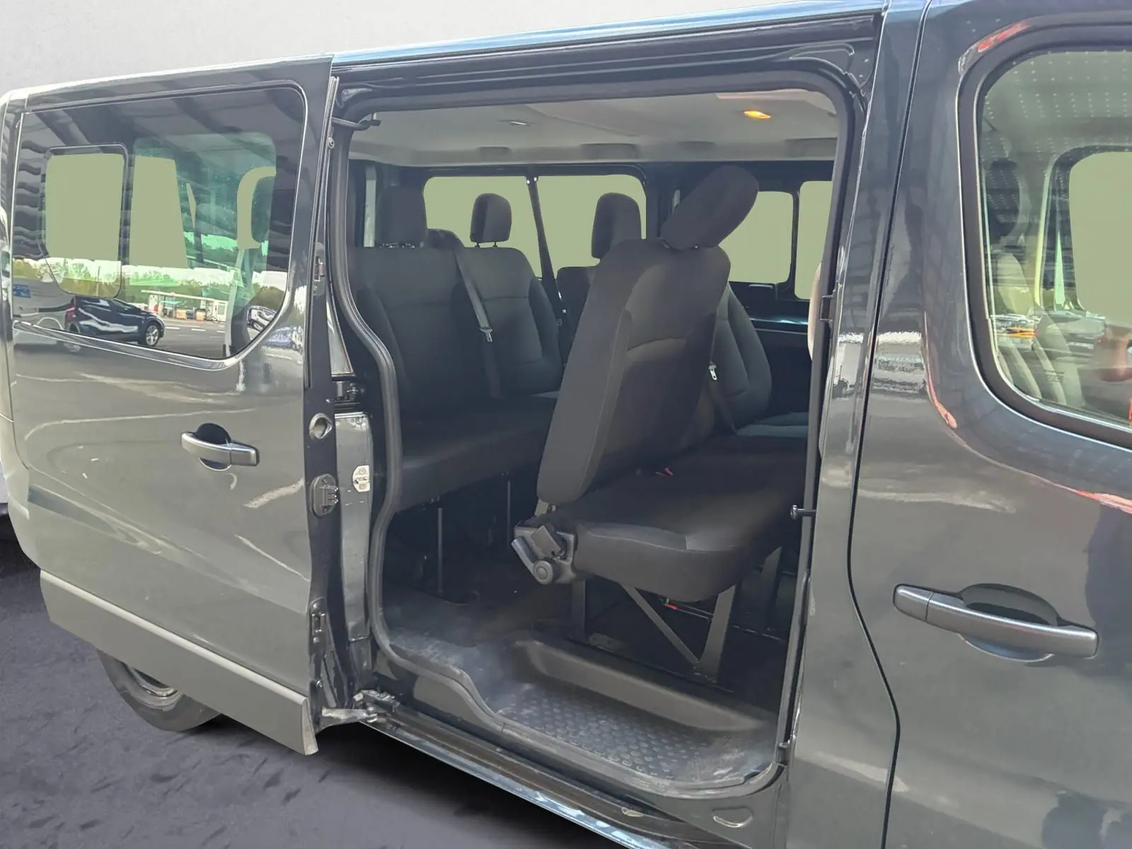 Vue latérale gauche du Renault Trafic Combi gris foncé avec porte coulissante ouverte révélant les sièges passagers noirs.