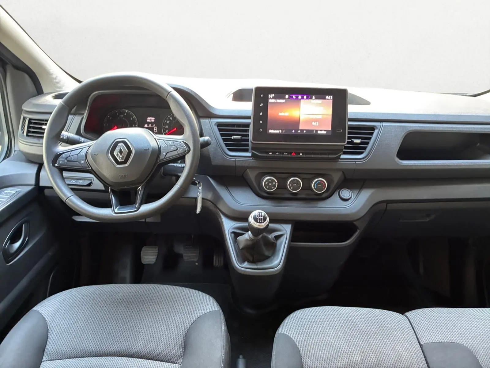 Vue frontale de l'intérieur du Renault Trafic Combi 2023, tableau de bord avec écran tactile et volant multifonction.
