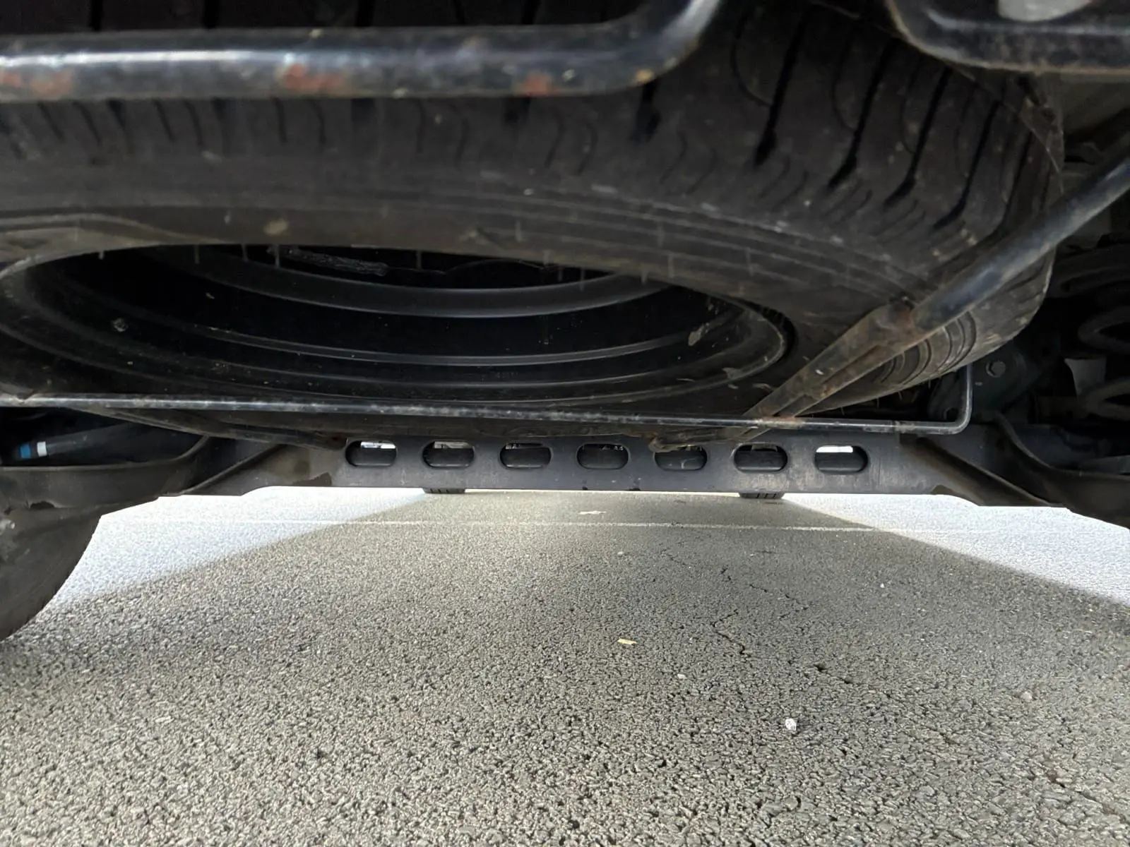 Vue en contre-plongée sous un Renault Trafic Combi gris foncé, montrant la roue de secours et le châssis métallique.