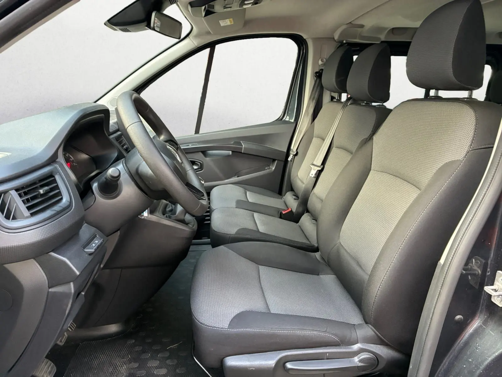 Vue intérieure côté conducteur du Renault Trafic Combi 2023, sièges tissu gris et tableau de bord noir.