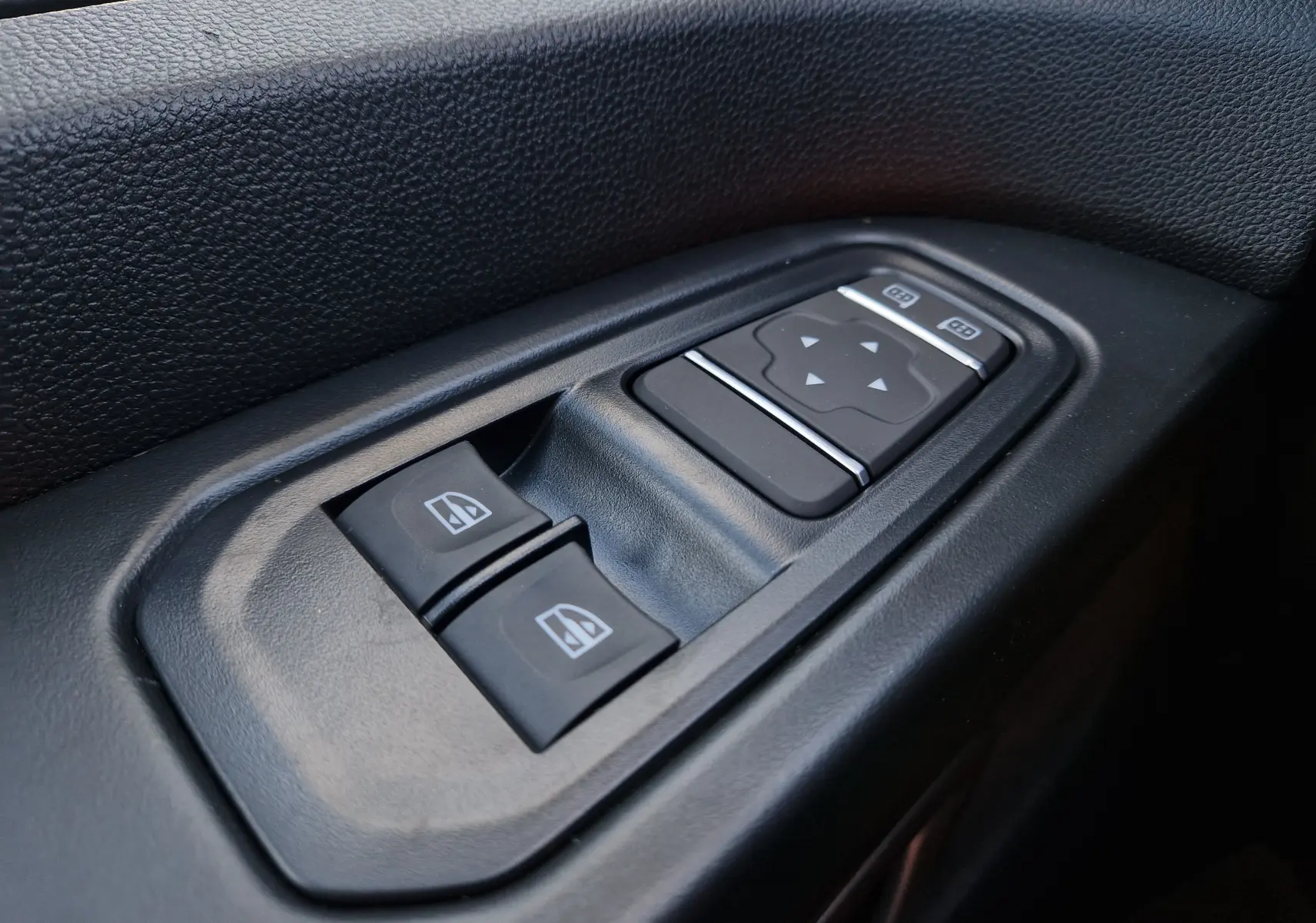 Gros plan sur les commandes de lève-vitres et réglage des rétroviseurs côté conducteur du Renault Trafic Fourgon blanc.