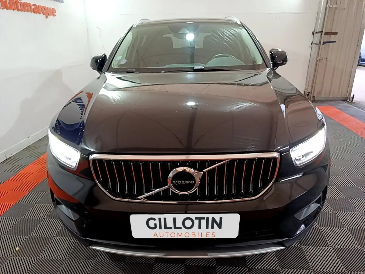 Vue frontale d'un Volvo XC40 noir avec calandre verticale chromée et phares LED allumés en intérieur showroom.