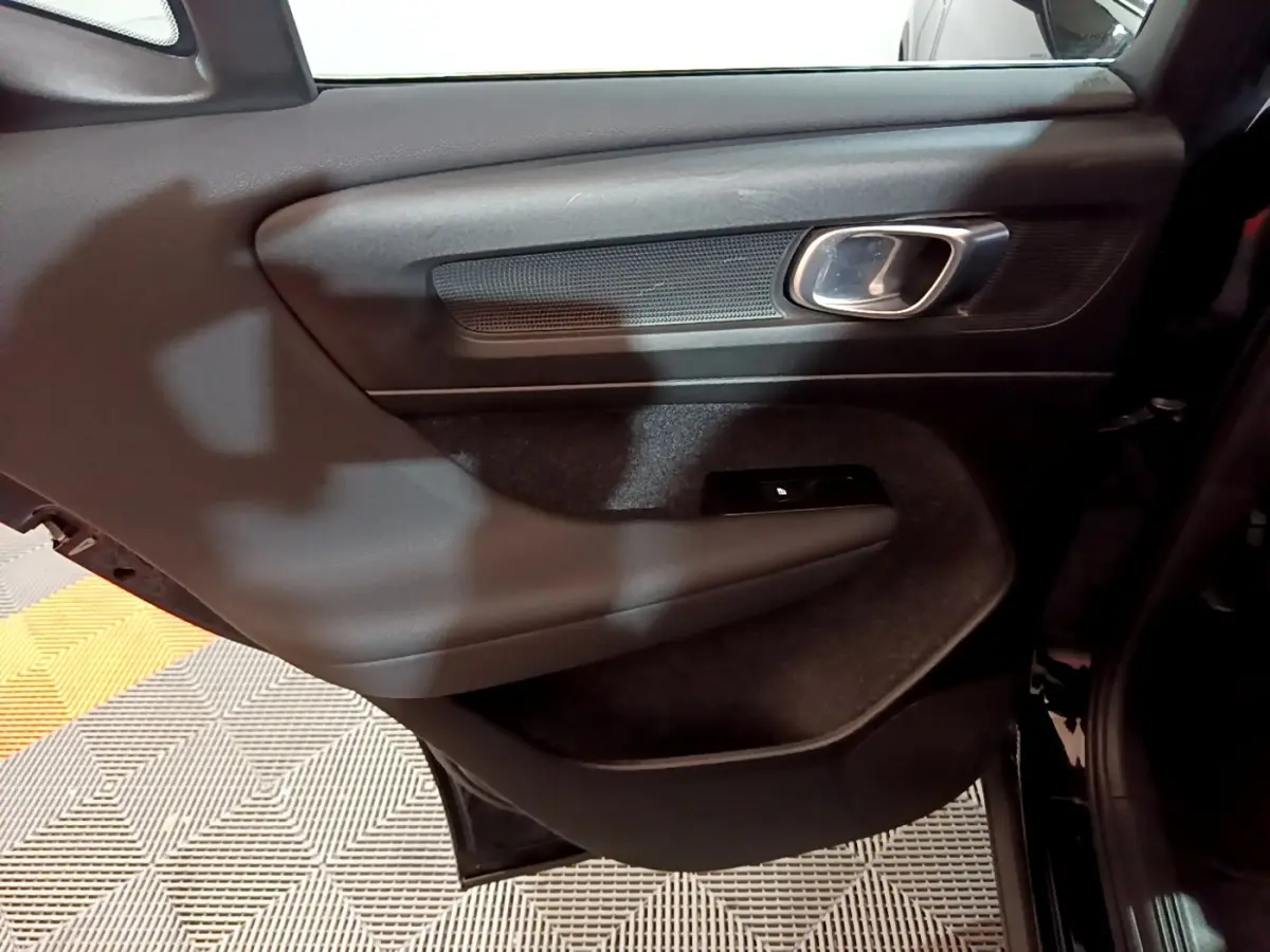 Gros plan sur la porte arrière gauche noire du Volvo XC40 Recharge T4 avec poignée chromée et commande de vitre.