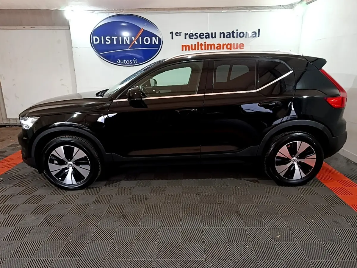 Profil côté gauche d'un Volvo XC40 noir hybride rechargeable, avec jantes modernes et lignes épurées en intérieur showroom.