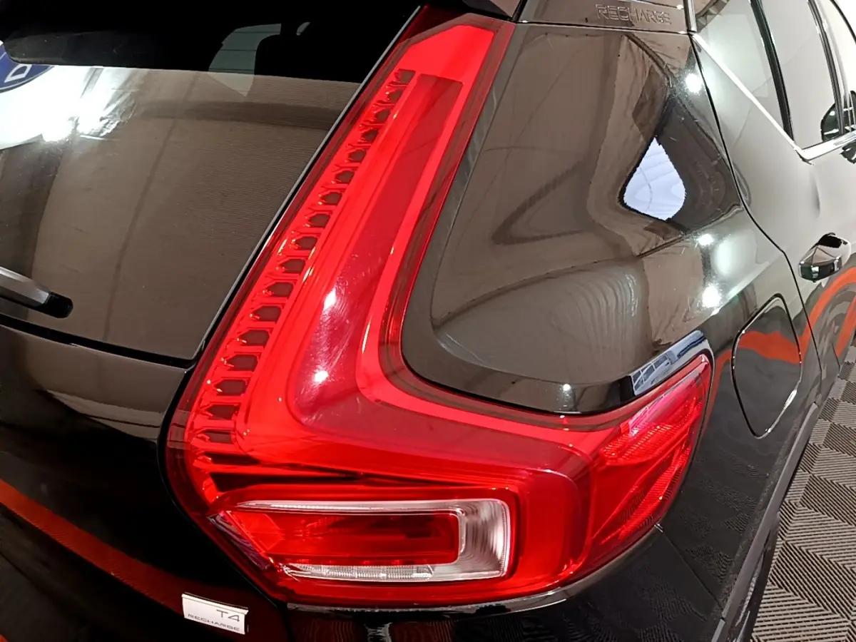Gros plan sur le feu arrière droit rouge vif d’un Volvo XC40 Recharge T4 noir brillant, avec reflet du plafond visible.