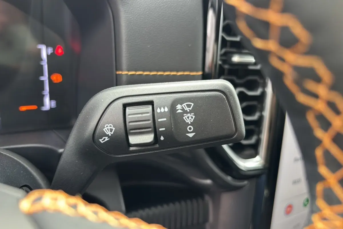 Gros plan sur la manette de commande des essuie-glaces du Ford Ranger Wildtrak Plus 2025, volant cuir noir avec surpiqûres orange.