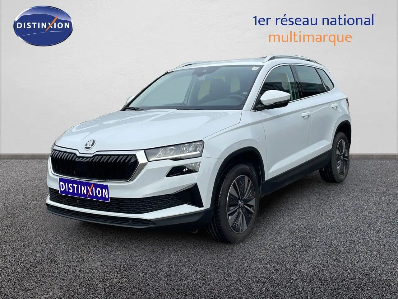 Vue 3/4 avant d’un Skoda Karoq blanc glacier avec calandre noire et jantes bi-ton, sur fond neutre extérieur.
