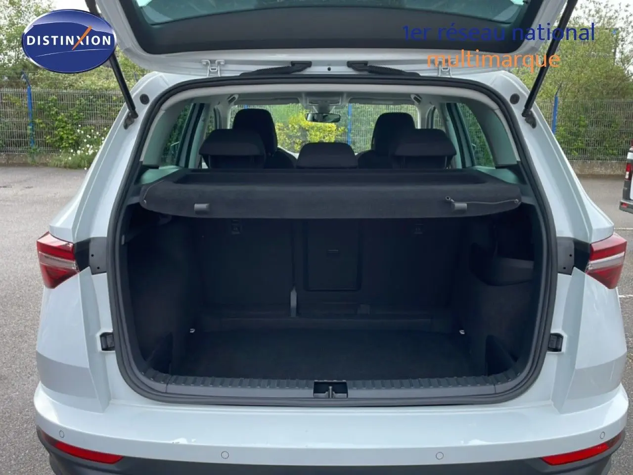 Vue arrière ouverte du coffre d’un Skoda Karoq blanc glacier 2025, montrant l’espace de chargement vide et la plage arrière noire.