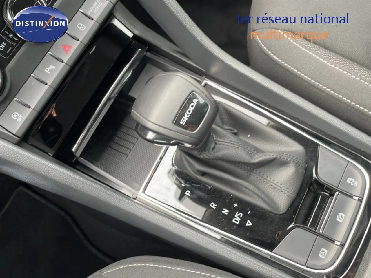 Gros plan sur le levier de vitesse automatique SKODA dans l’habitacle du KAROQ, avec sellerie tissu gris et coutures blanches.