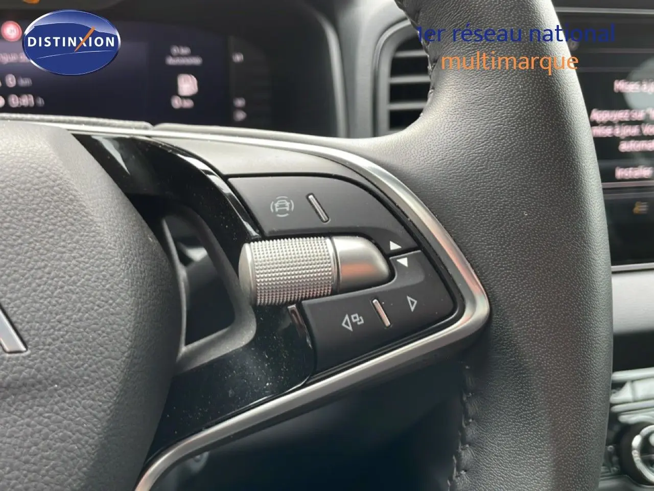 Gros plan sur les commandes au volant cuir noir du Skoda Karoq blanc glacier, avec tableau de bord numérique en arrière-plan.