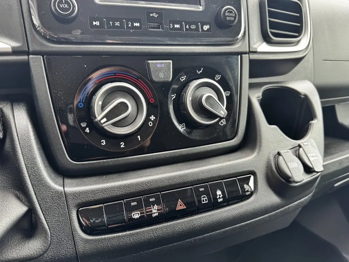 Gros plan sur la console centrale noire du Peugeot Boxer Fourgon 2026, montrant les commandes de climatisation et les prises USB et 12V.