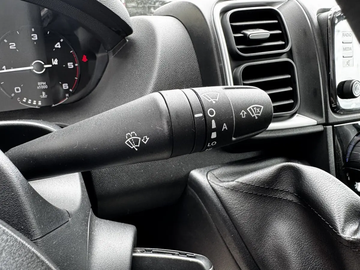 Gros plan sur la manette d’essuie-glace noire du tableau de bord du Peugeot Boxer Fourgon blanc, intérieur avant.