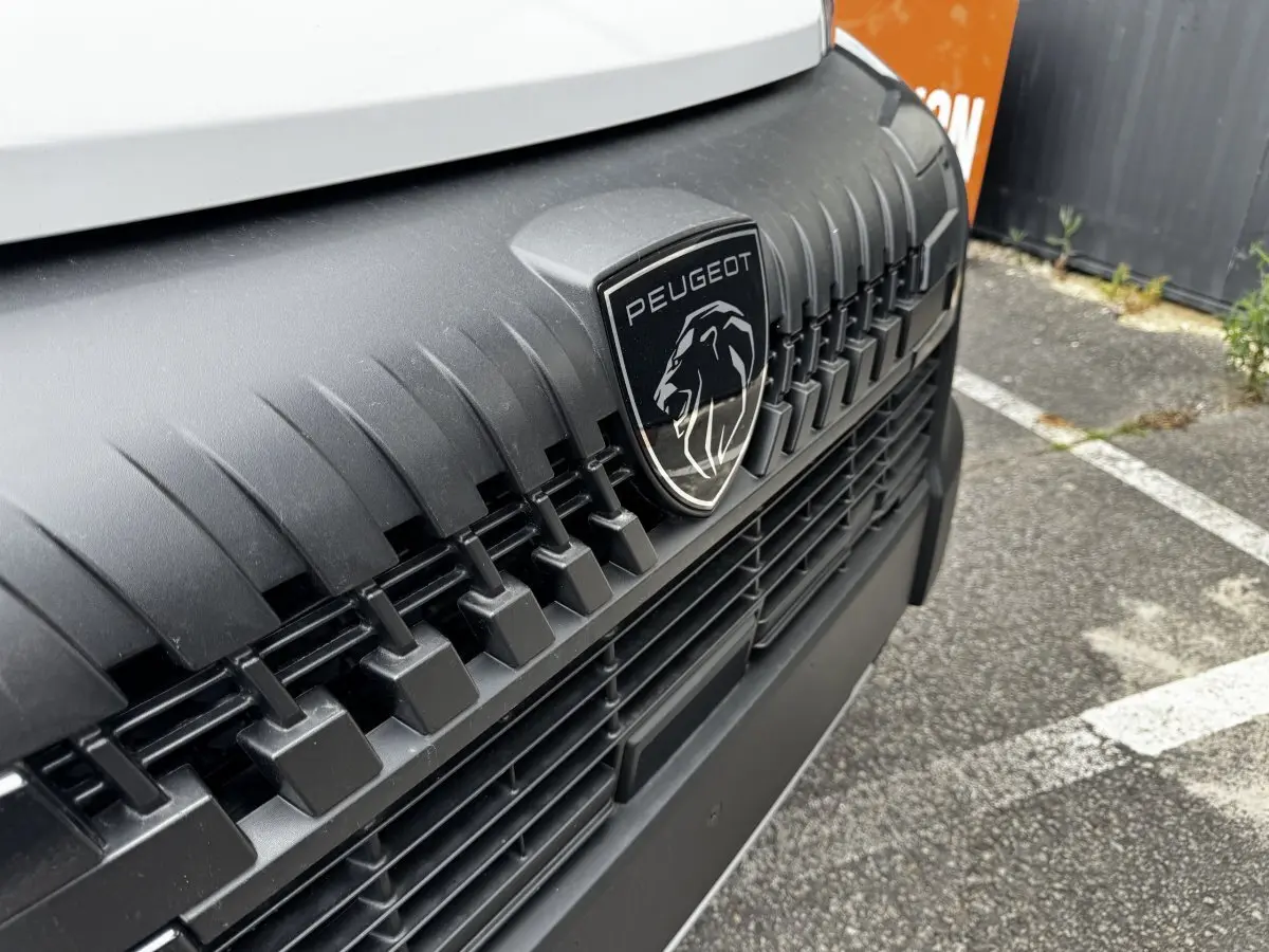 Gros plan sur la calandre noire et le logo Peugeot du Peugeot Boxer Fourgon blanc, vue avant rapprochée.