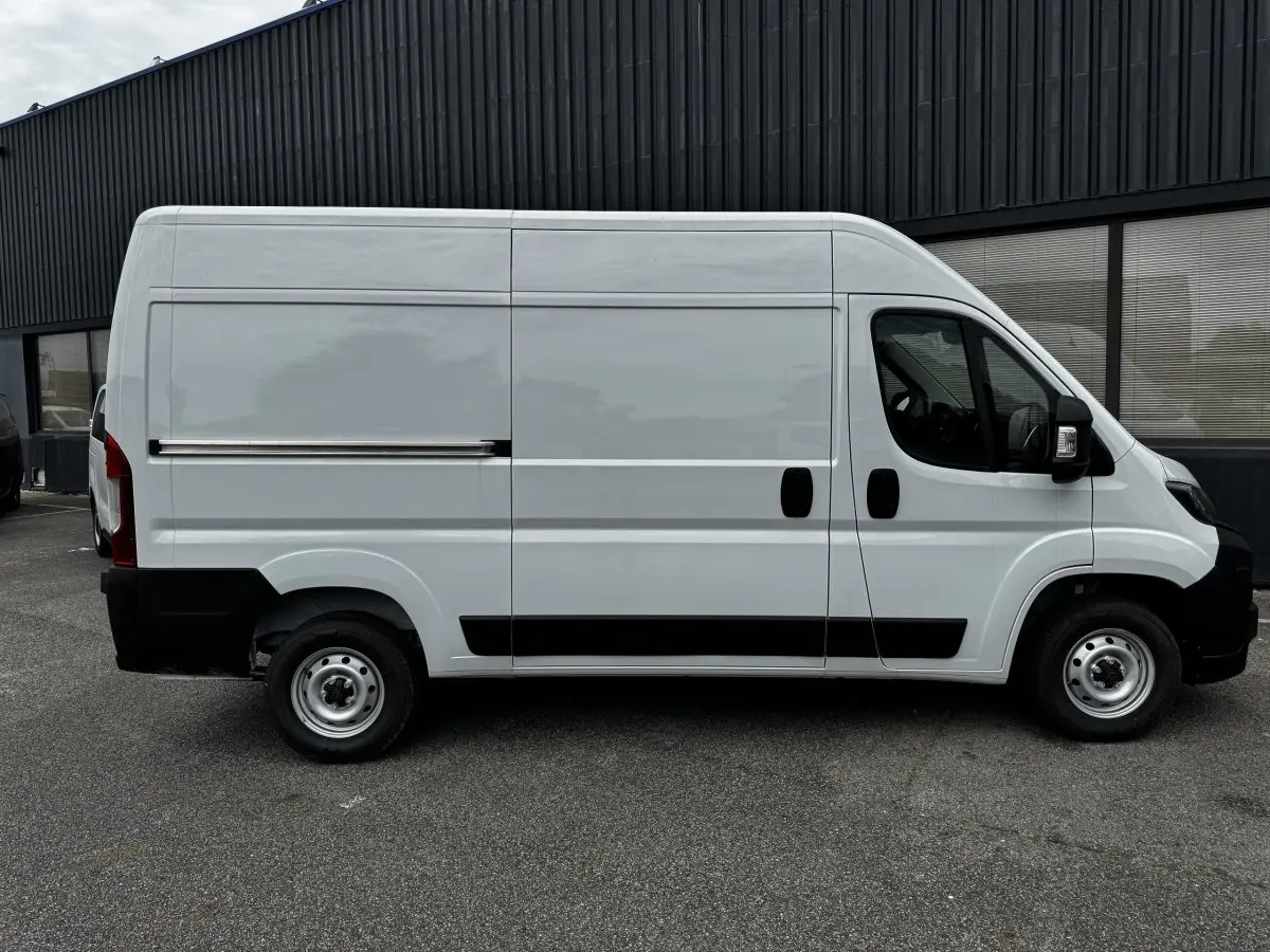 Vue de profil côté gauche d’un Peugeot Boxer Fourgon blanc avec porte coulissante et protections noires sur un parking.